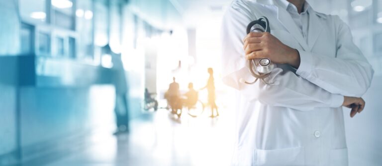 Medico in camice bianco in un corridoio ospedaliero luminoso.